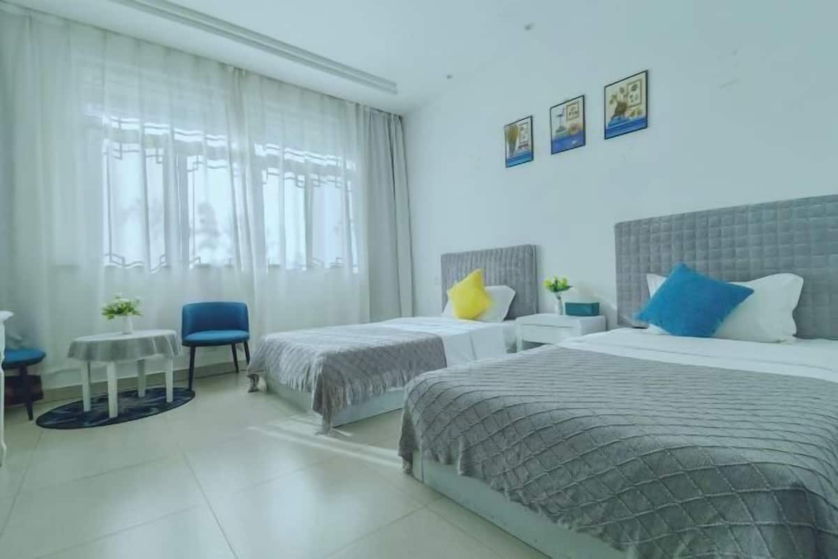 A hotel room with two beds, a chair, a small table, and a window with curtains.