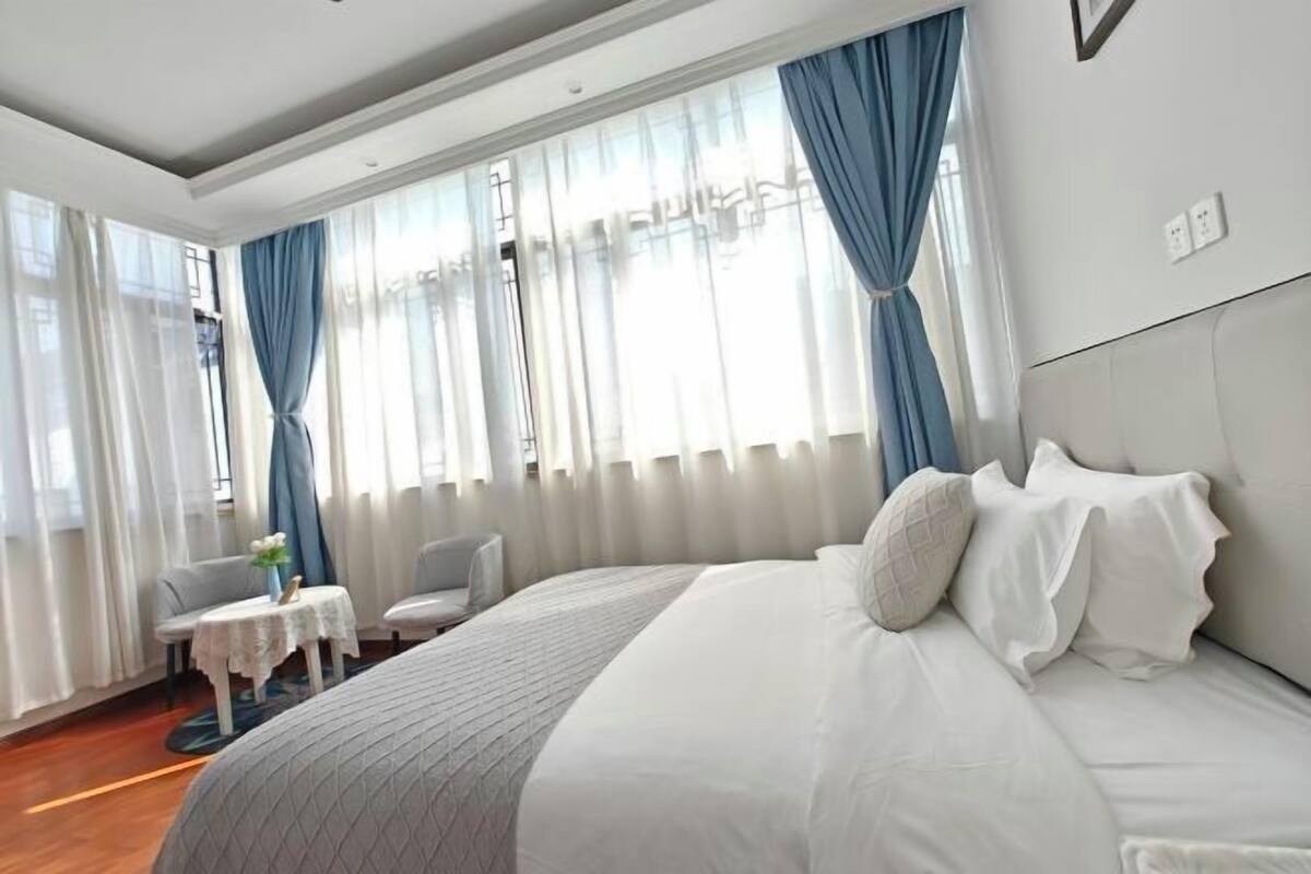 A hotel room with a large bed, a small table with a vase, and a chair.