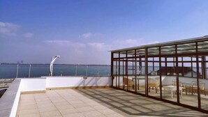 Een terras op het dak met een glazen overkapping, buitenmeubels en uitzicht op de zee.