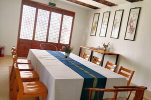 Un comedor con una larga mesa, sillas, un jarrón con flores y cuadros en la pared.
