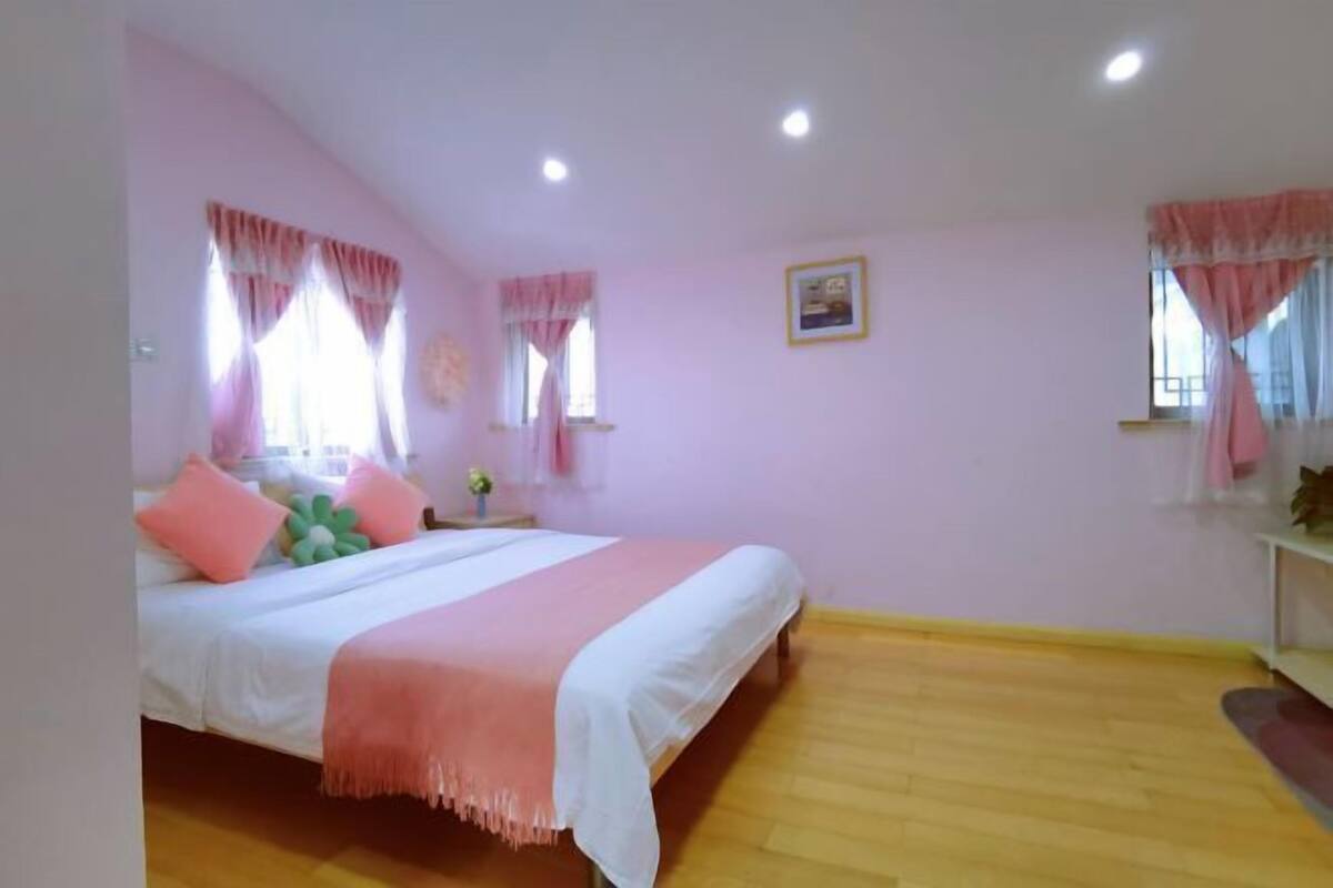 A bedroom with a bed, two windows with curtains, a bedside table, and a wall-mounted picture.