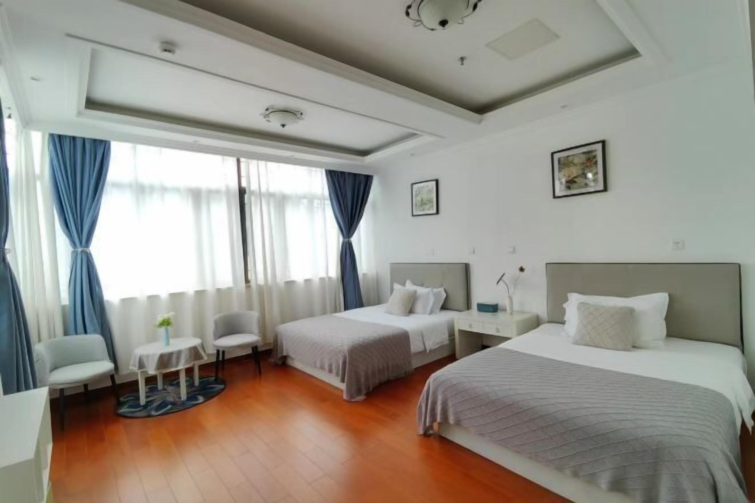 Une chambre d’hôtel avec deux lits, une petite table, une chaise et une fenêtre avec des rideaux.