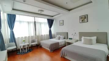 Une chambre d’hôtel avec deux lits, une petite table, une chaise et une fenêtre avec des rideaux.