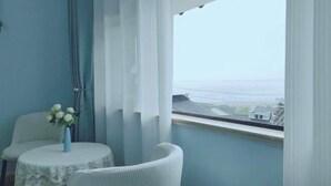 Een kamer met uitzicht op een brug, een stoel, een klein tafeltje met een bloemenvaas en een raam met gordijnen.