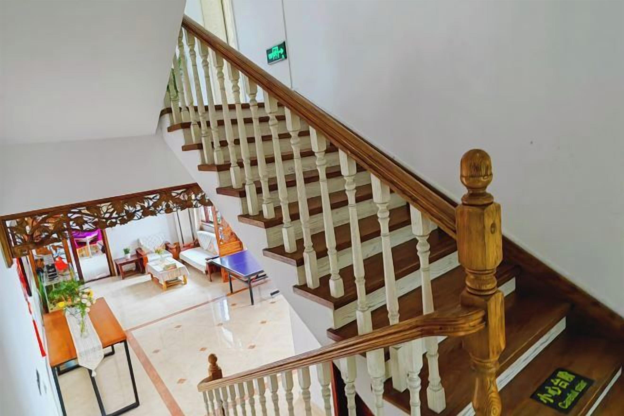 A staircase with wooden balusters and a handrail, leading to a room with a bed, a table, and a chair.
