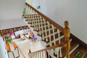 Un escalier avec des balustrades en bois et une main courante, menant à une pièce où se trouvent un lit, une table et une chaise.