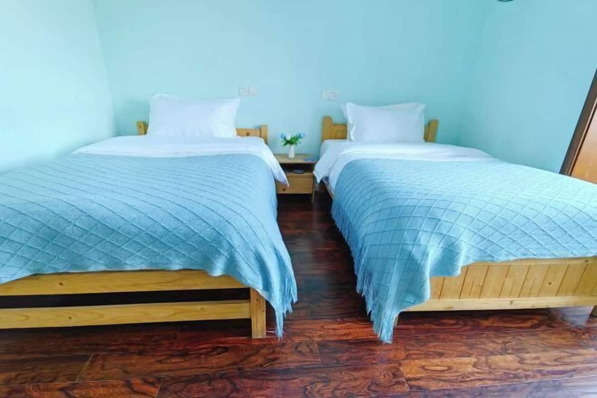 A room with two wooden beds, each with a blue quilted bedspread and white pillows.