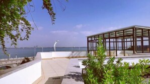 Een terras op het dak met een glazen omheining, uitzicht op zee en een heldere lucht.