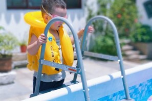 Un nen amb un salvavides groc dempeus sobre una escala de piscina.