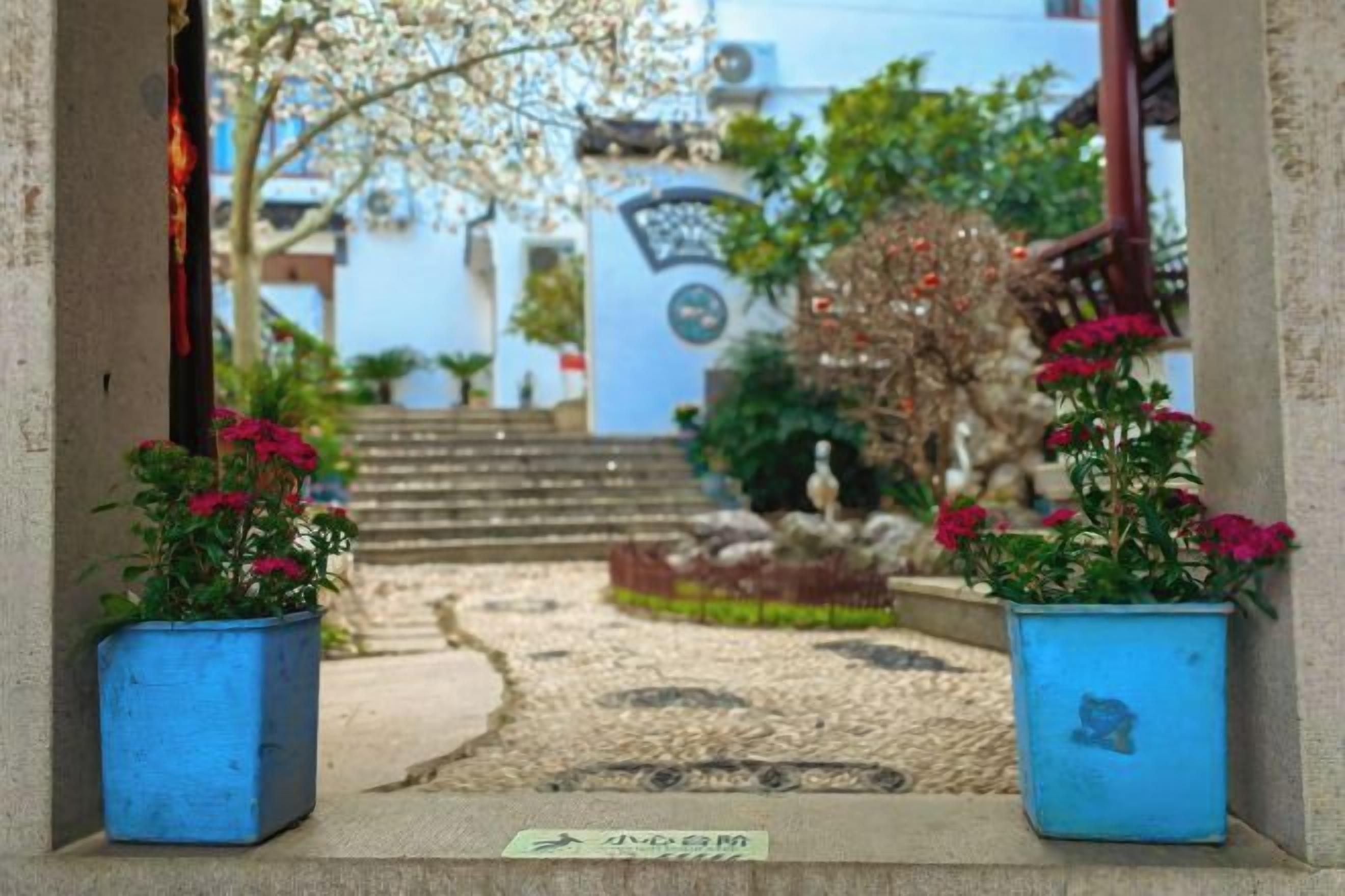 A pathway leading to a building with steps, potted plants, and a sign.