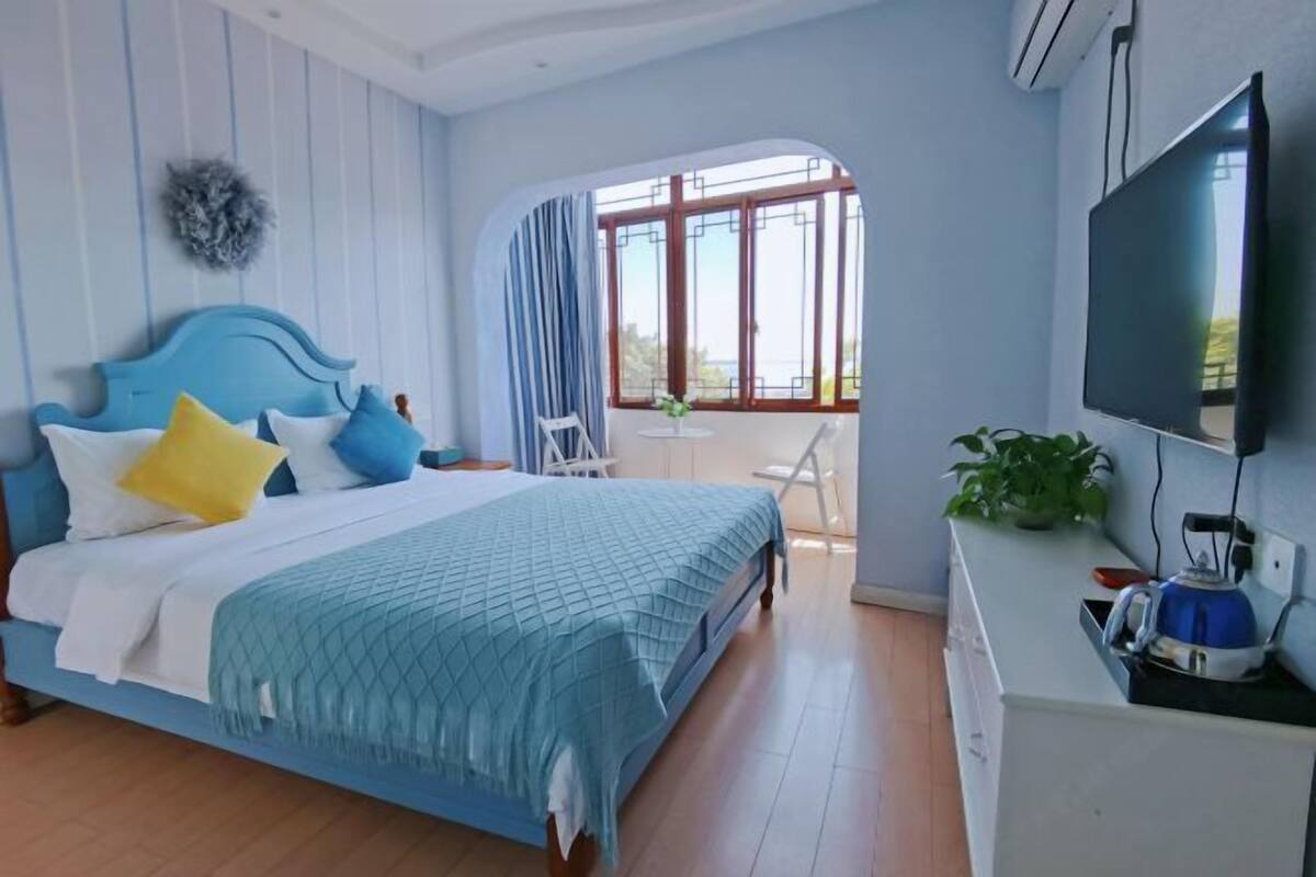 A bedroom with a bed, a TV, a window, and a plant.
