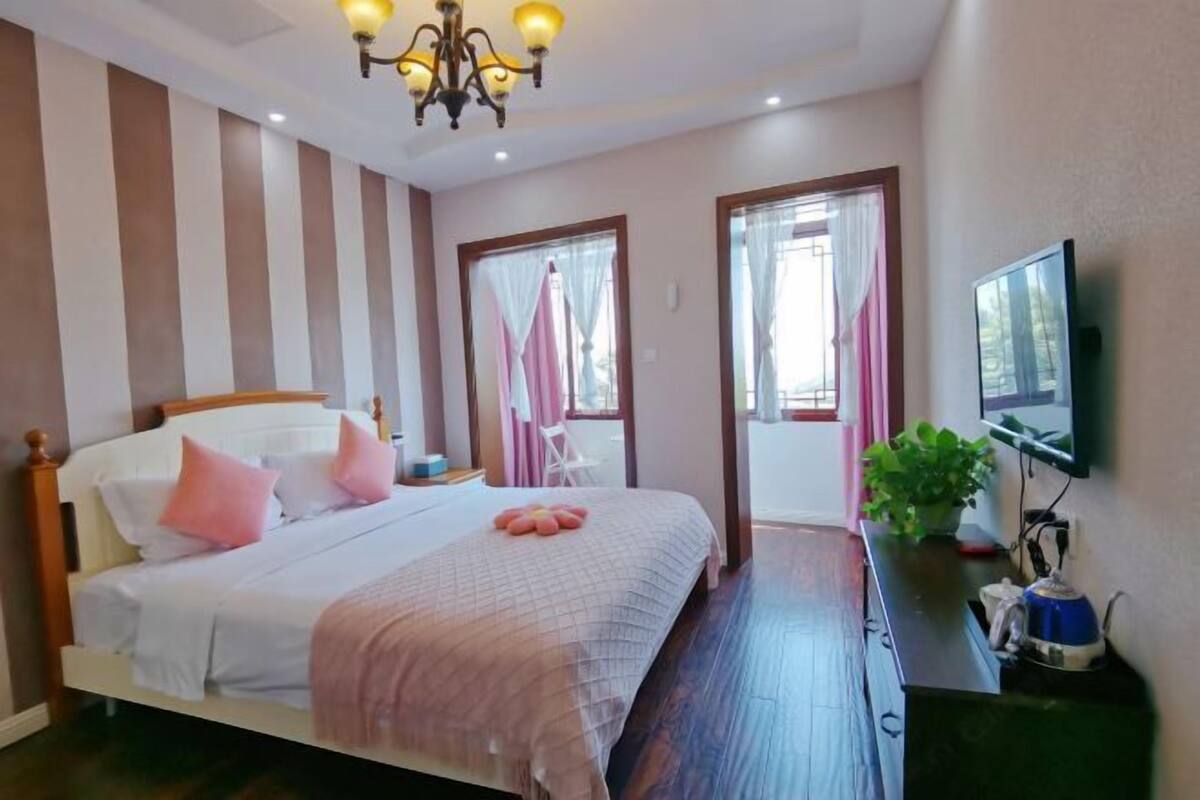 A hotel room with a bed, bedside table, TV, and a plant.