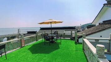 Una terraza en la azotea con una mesa, sillas, un paraguas grande y vista al mar.