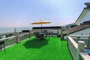 A rooftop terrace with a table and chairs, a large umbrella, and a view of the sea. - Jiusu Shanshuijian Guesthouse (Suzhou)