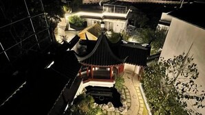 Een traditioneel Japans paviljoen met een betegeld dak, omgeven door een tuin met een grindpad en een kleine vijver.