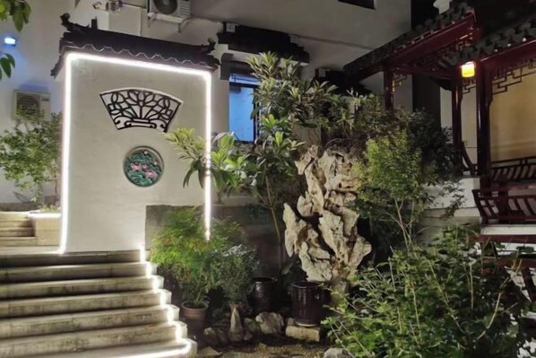 Un patio tradicional con una escalera de piedra, una formación rocosa y plantas en macetas.