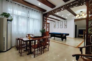 A dining area with a table and chairs, a refrigerator, and a pool table. - Jiusu Shanshuijian Guesthouse (Suzhou)