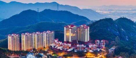 A high-rise residential building complex with multiple apartment buildings, surrounded by lush greenery and mountains in the background.