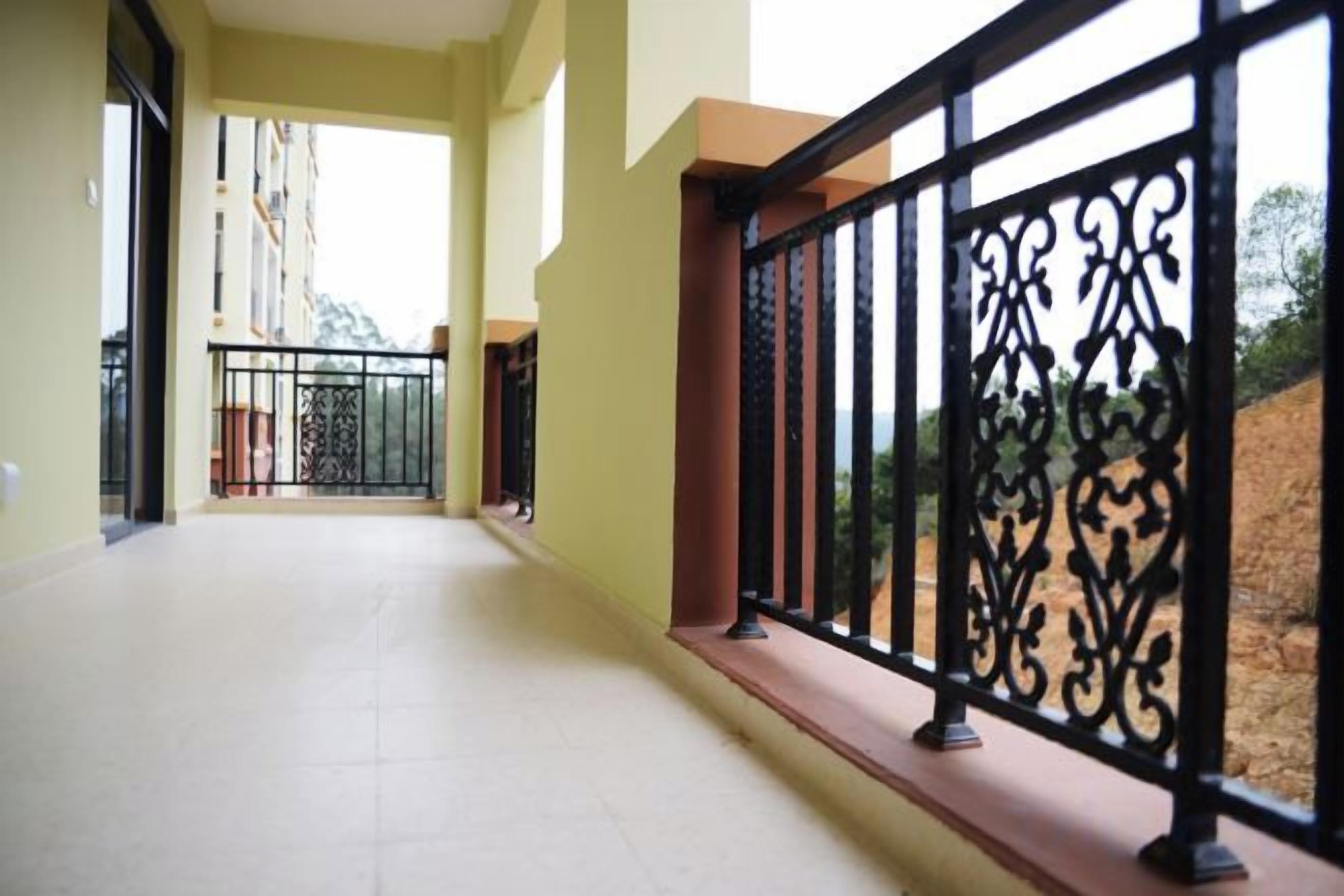 A corridor with a tiled floor, a black wrought iron balcony railing, and a view of a building and trees.
