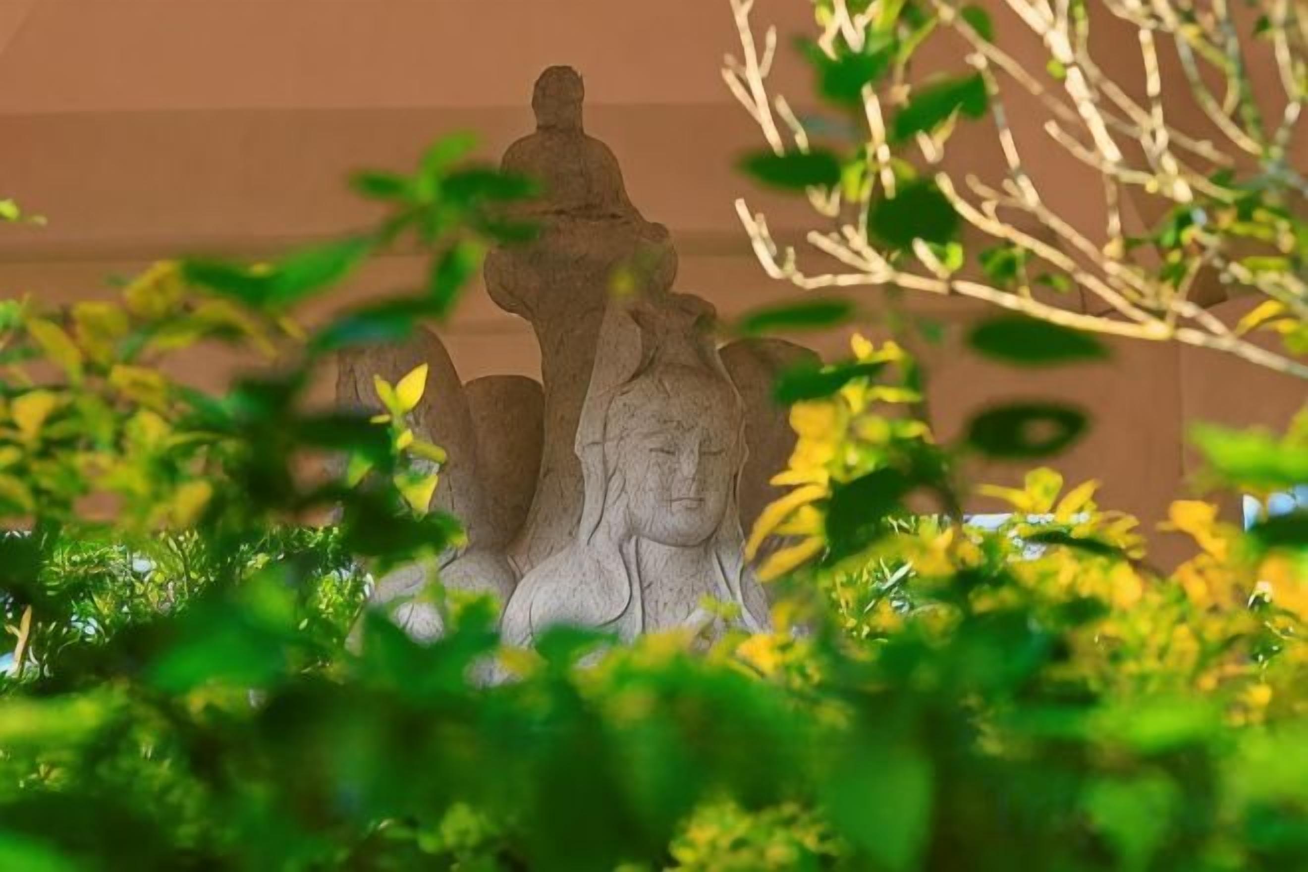 A stone statue partially obscured by foliage.