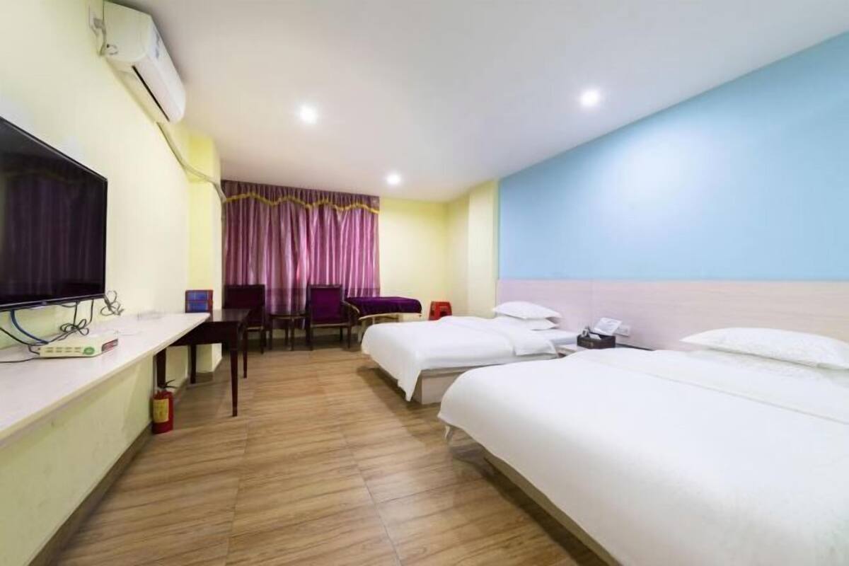 A hotel room with a bed, a desk with a television, a chair, a small table, and a window with curtains.
