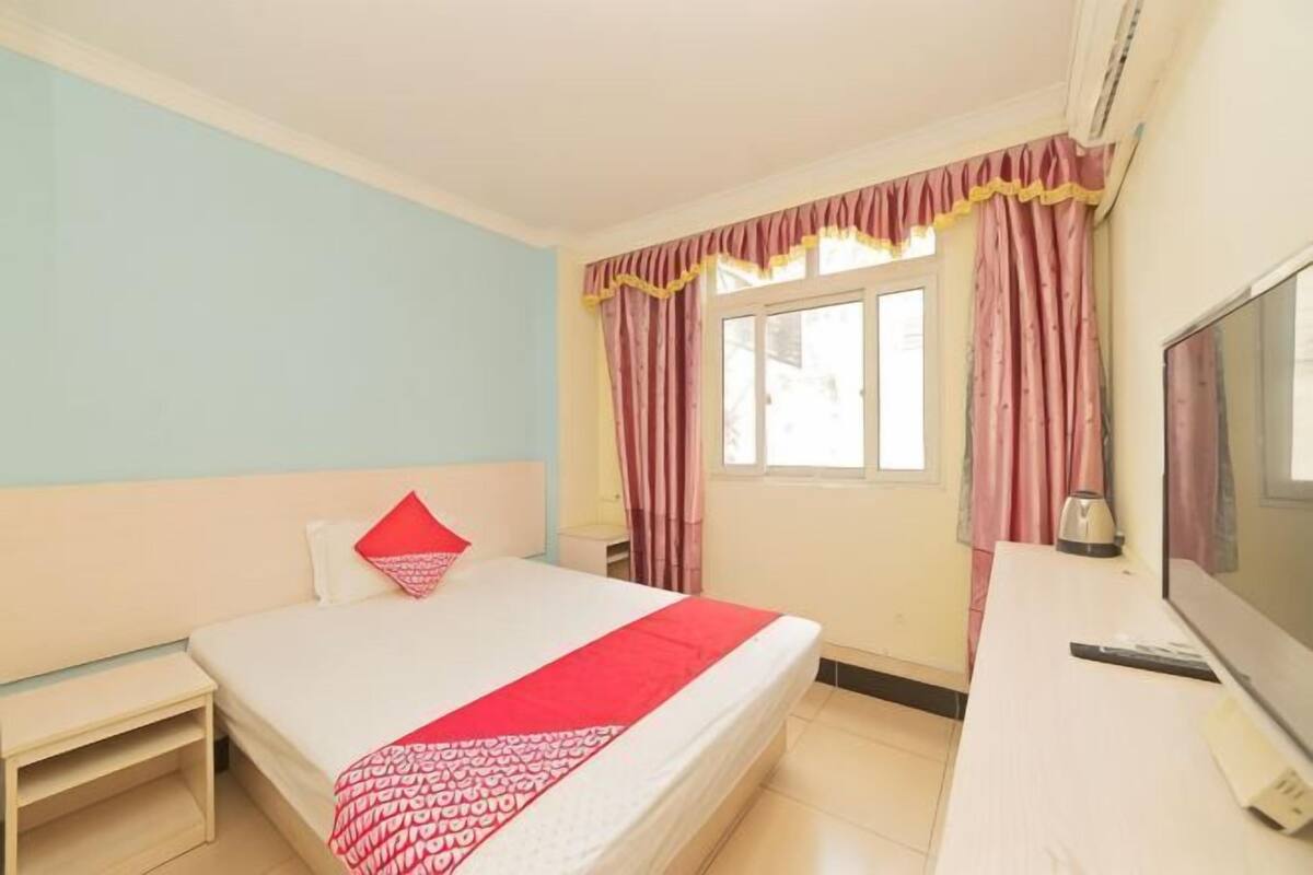 A hotel room with a bed, a desk, a TV, and a window with curtains.