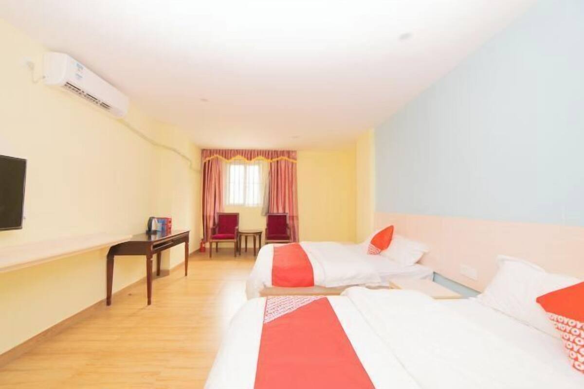 A hotel room with two beds, a desk, a chair, a TV, and a window with curtains.