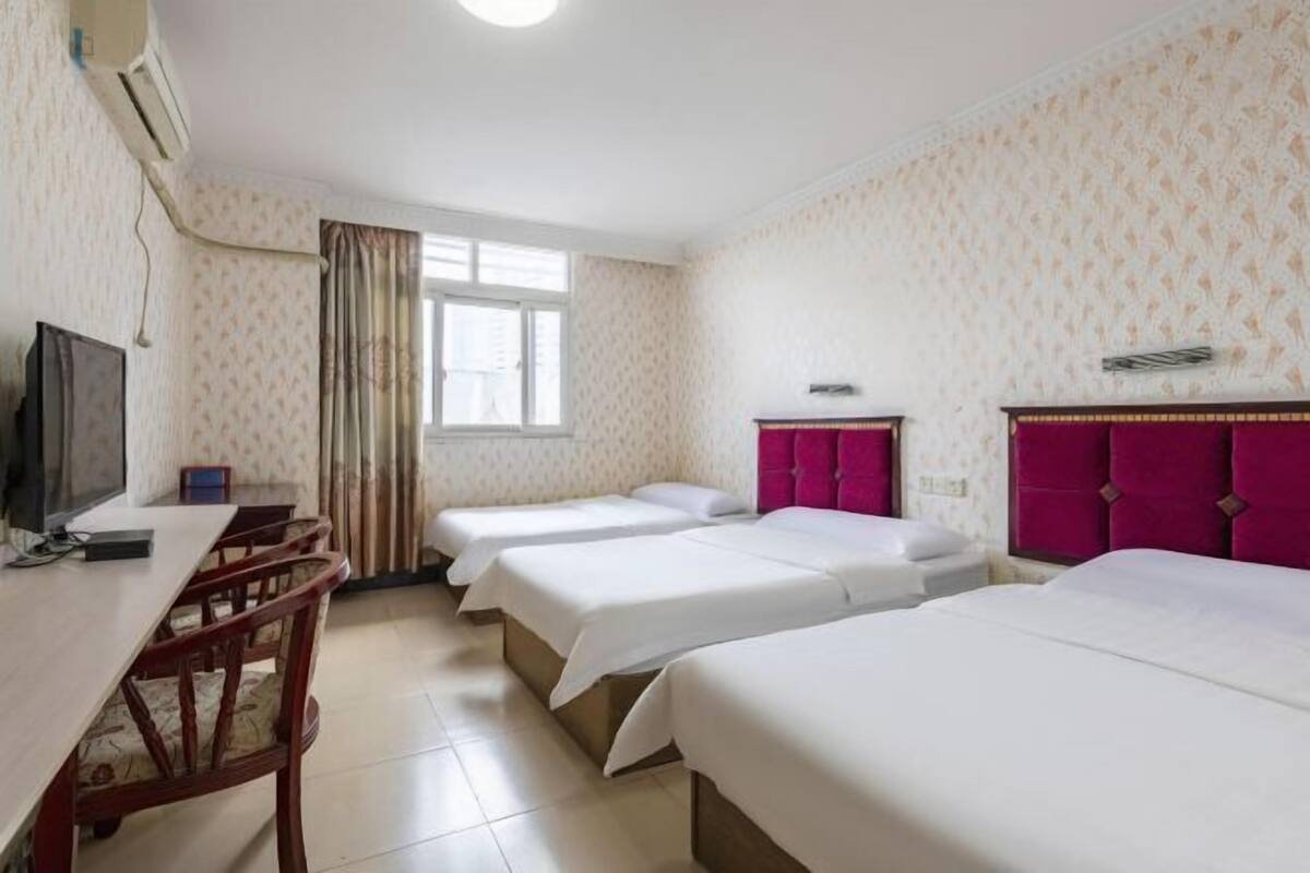 A hotel room with three beds, a TV, a desk, and a window with curtains.