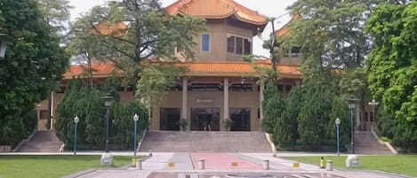 A traditional building with a tiled roof, a central entrance, and a paved area with bollards in front.