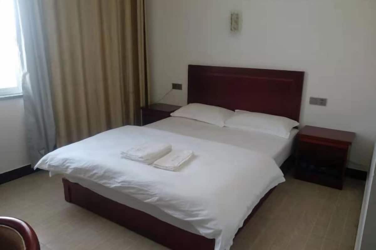 Une chambre d’hôtel avec un lit simple, deux tables de chevet, une fenêtre avec des rideaux et un mur uni.