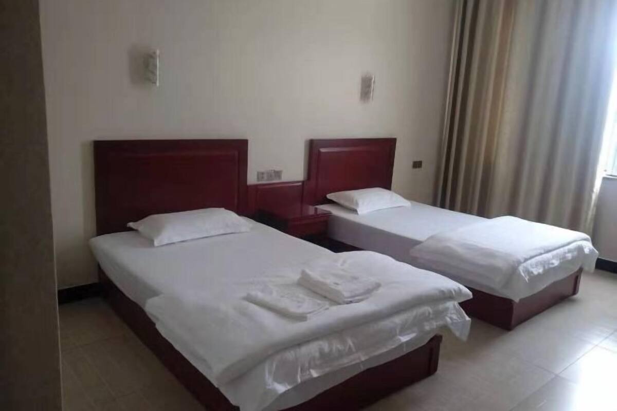 Deux lits simples avec des têtes de lit en bois, du linge de lit blanc et une table de chevet placée entre les deux.