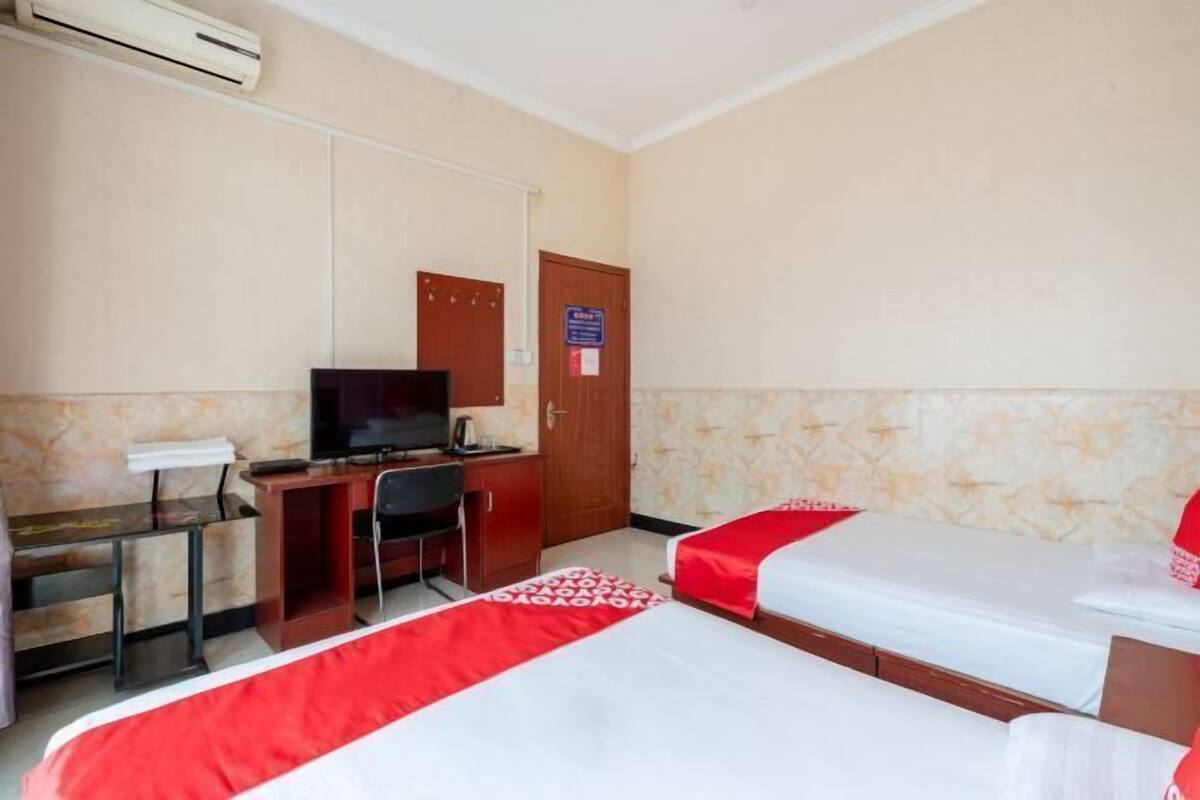 A hotel room with two beds, a desk with a chair, a television, and an air conditioning unit.