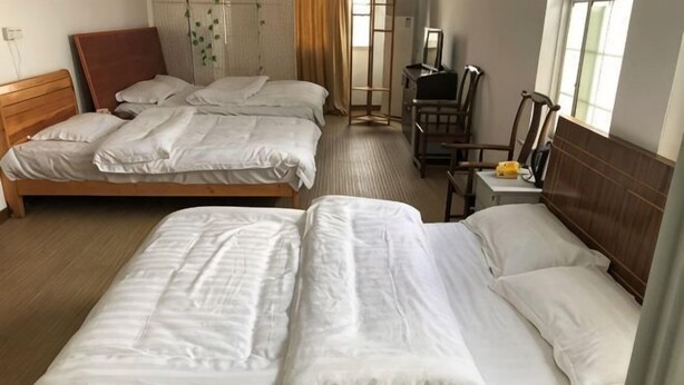 A hotel room with two beds, a wooden headboard, a desk with a chair, and a window with curtains. - Feiyu Hostel (Shanghai)
