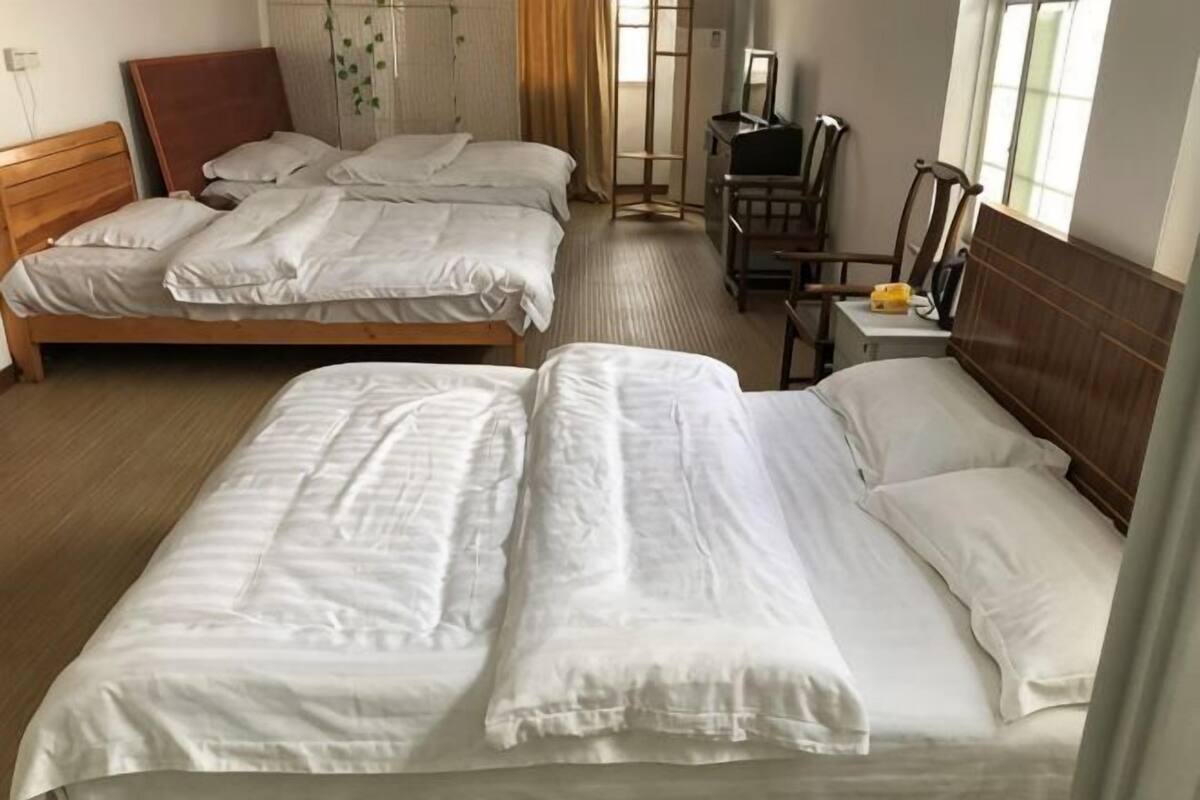 A hotel room with two beds, a wooden headboard, a desk with a chair, and a window with curtains.
