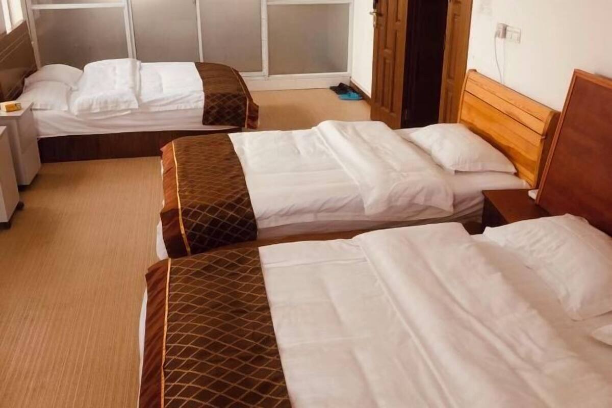 A hotel room with two beds, a wooden headboard, a bedside table, and a window.