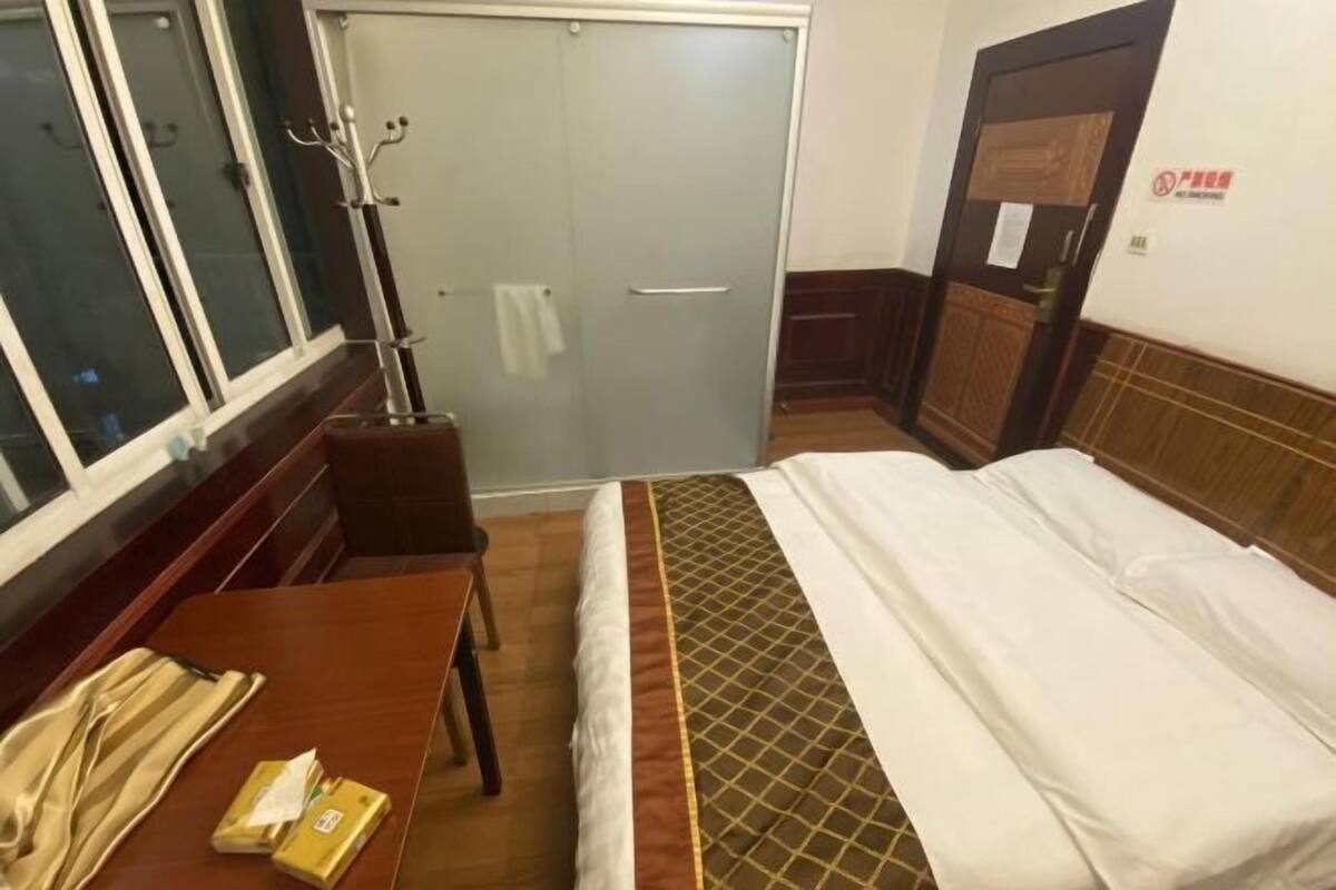 A hotel room with a bed, a wooden table, a chair, a coat rack, and a sliding door.