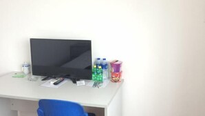 A white desk with a black monitor, a blue chair, and various items including bottles and a cup. - Feiyu Hostel (Shanghai)