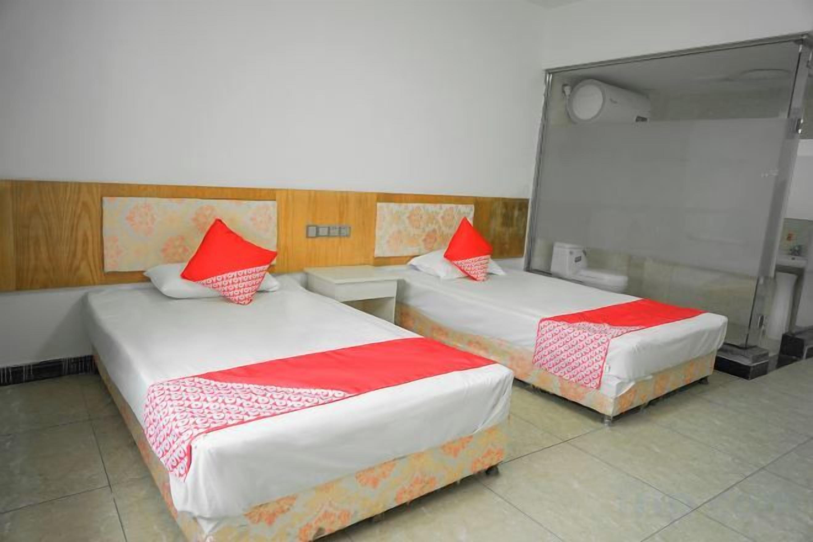 Two single beds with red pillows, a wooden headboard, a small bedside table, and a shower area.