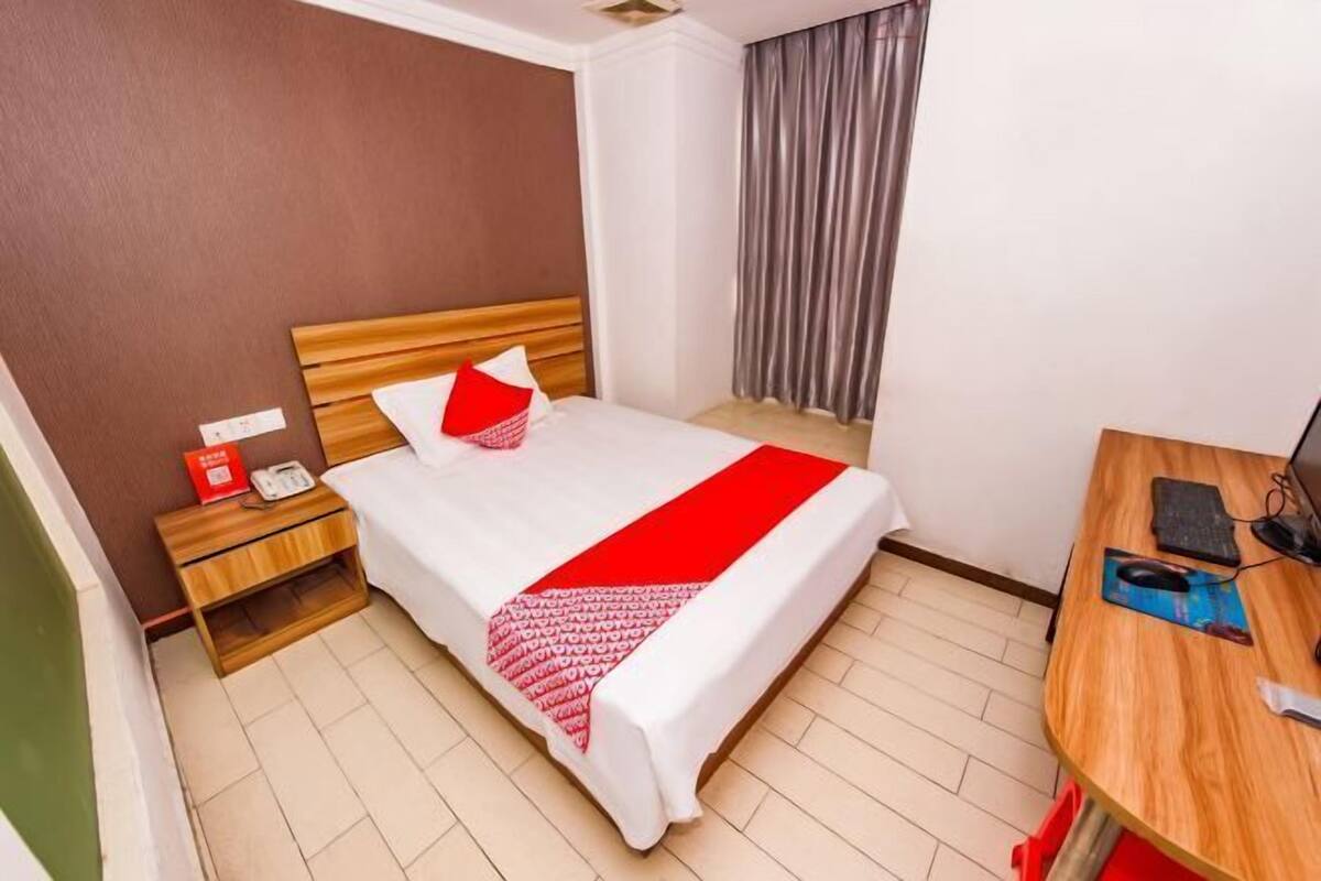 A hotel room with a bed, bedside table, and a desk with a computer.