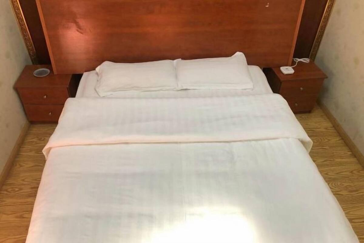 A neatly made bed with white linens and a wooden headboard. There are two bedside tables with a small lamp and a power outlet on each.