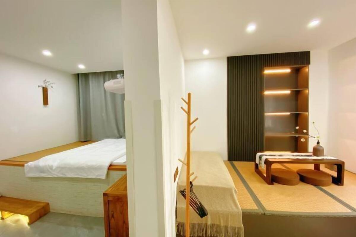 A minimalist room with a bed, a small table with a bench, and a shelf with storage.