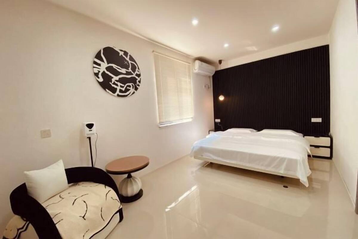 A modern bedroom with a bed, a round table, and a wall-mounted artwork.