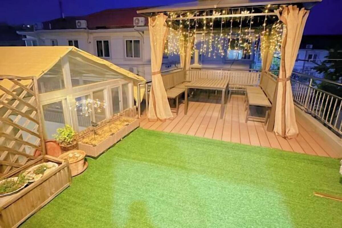 A rooftop terrace with a greenhouse, seating area, and string lights.