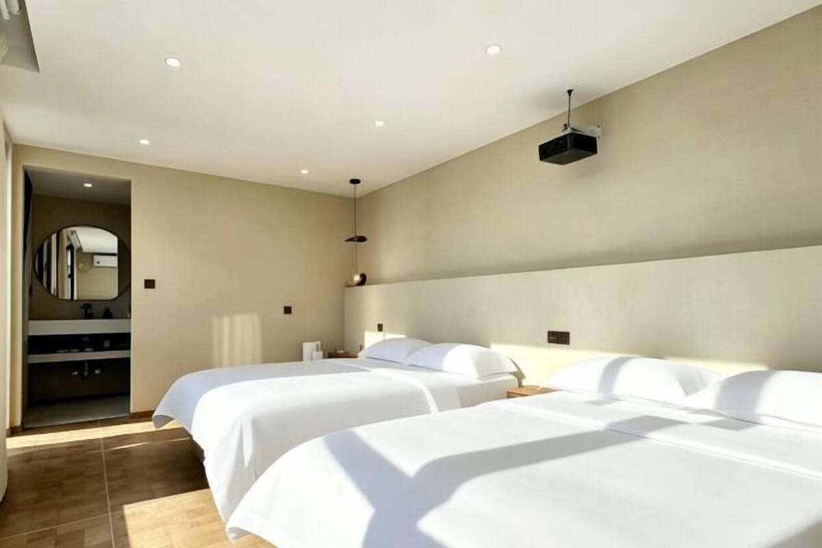 A hotel room with two beds, a large mirror, a TV, and a small bathroom.