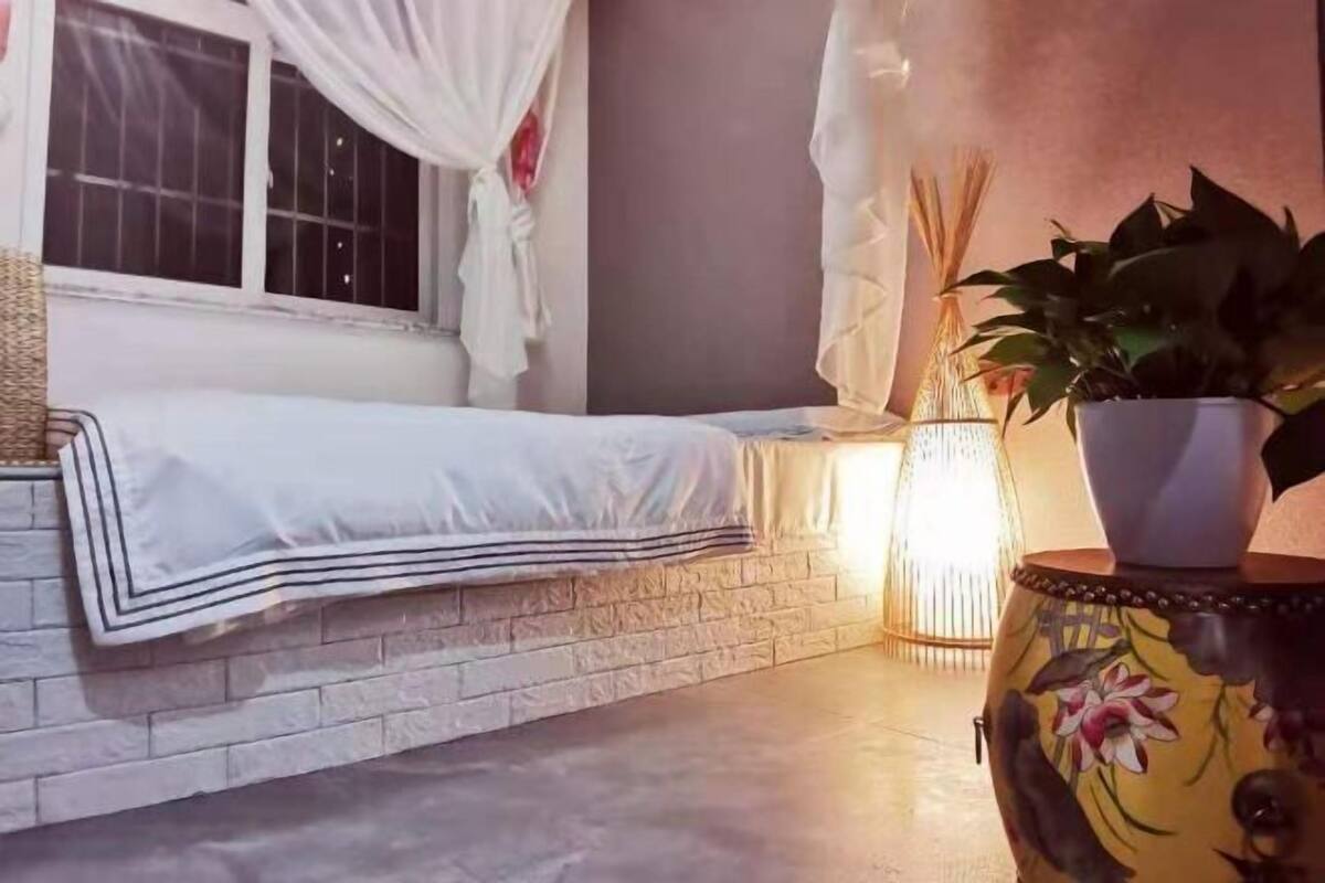 A room with a bed, a window with curtains, a potted plant, and a decorative vase.
