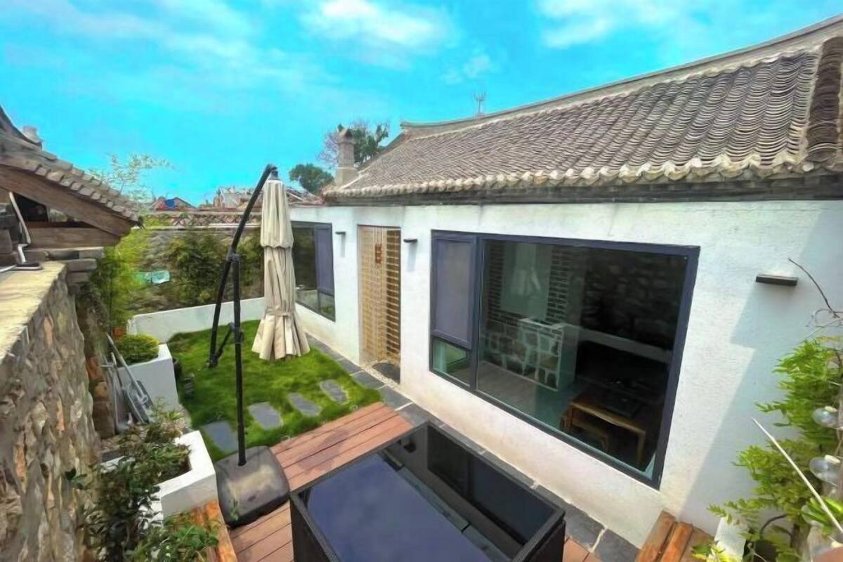 A traditional-style building with a tiled roof, large windows, and a small courtyard with a wooden deck and a hanging chair.
