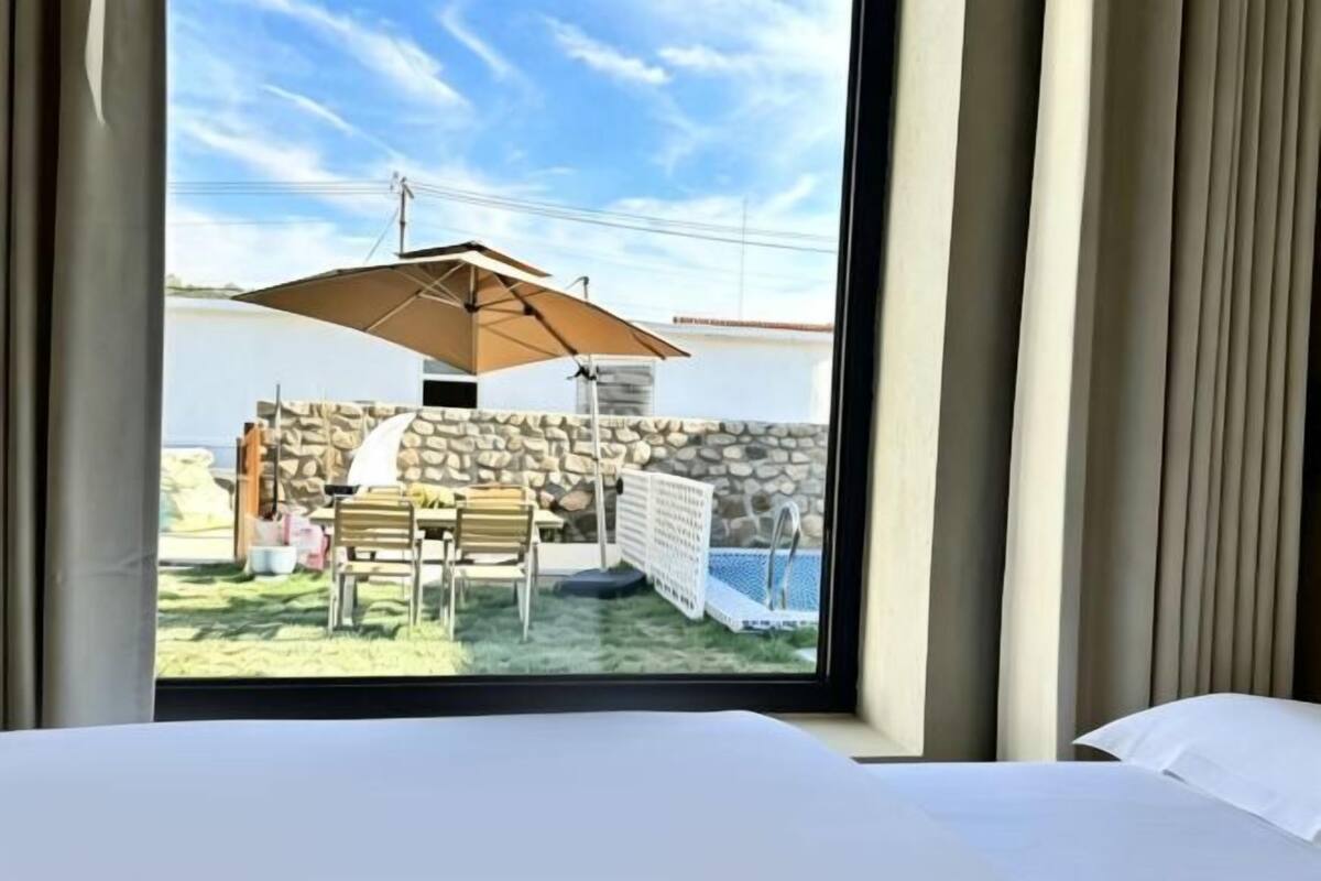 A hotel room with a bed, a window overlooking a patio with a table, chairs, and an umbrella.