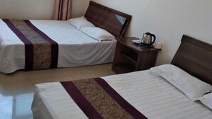 Habitación de hotel con dos camas individuales, una mesita de noche con hervidor y una ventana con cortinas.