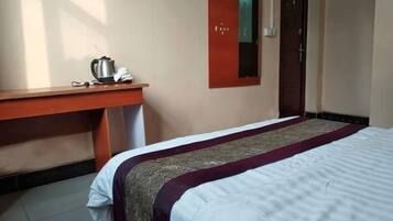 A hotel room with a bed, a wooden desk, a telephone, and a mirror.