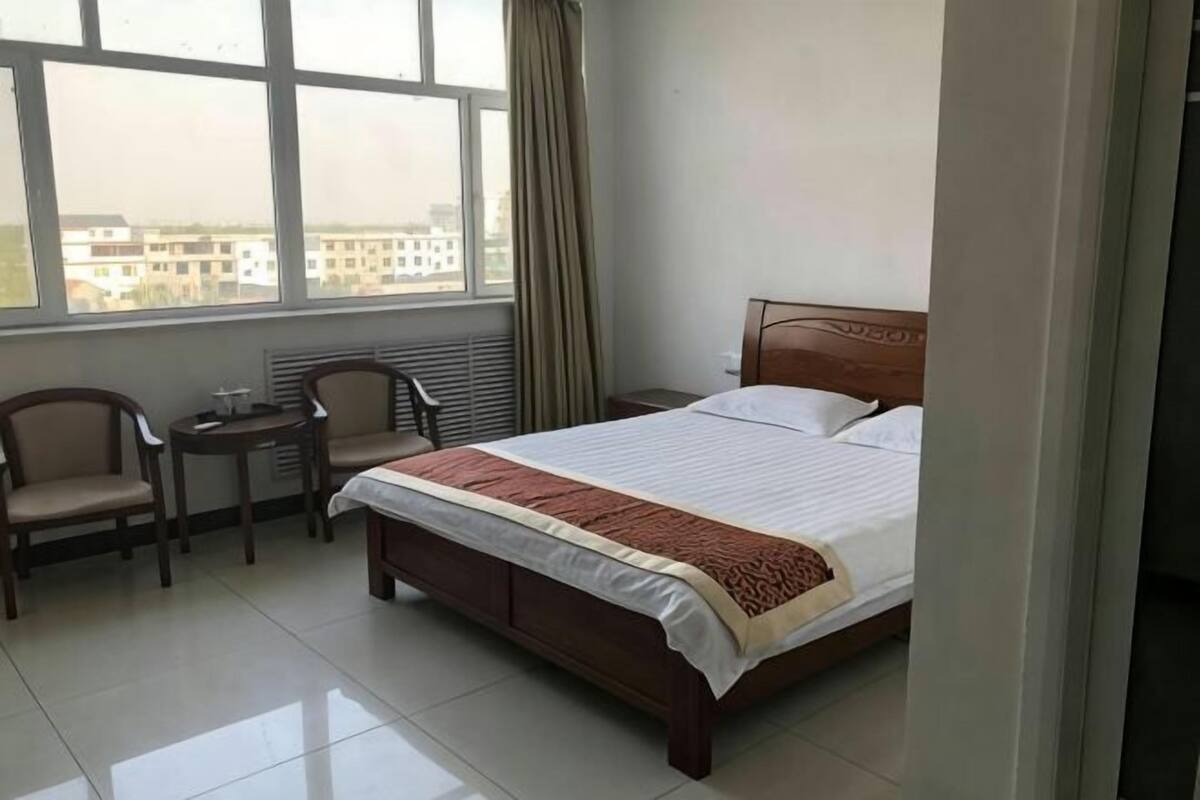 Une chambre d’hôtel avec un lit, un bureau, deux chaises et une fenêtre avec des rideaux.